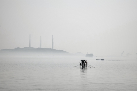 The view on the open sea with a small boat and factory's stalks in the background.の写真素材