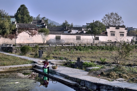 XIDI, ANHUI PROVINCE, CHINA  CIRCA OCTOBER 2017:  A woman washing the clothes in a bank of a pond in Xidi, a small ancient village in Anhui province in China near the Yellow Mountains.のeditorial素材