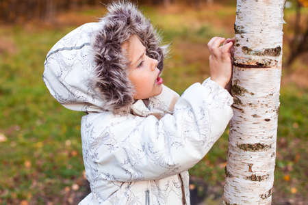 little girl walking in autumn forest in white clothes in road