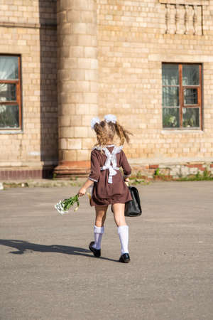 children in school uniforms with a briefcase walk and eat near the schoolの写真素材