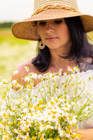 Beautiful young girl with curly red hair in camomile fieldの写真素材