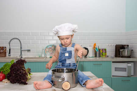 A cute little boy in a chefs costume cooks food with emotionsの写真素材
