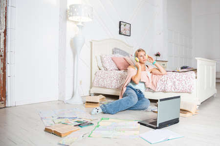 A blonde woman is sitting near the bed with a laptop and headphones