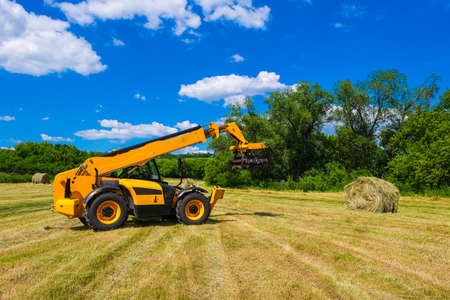 A ranch worker moving bales of hay with a farm tractor on a ranchの写真素材