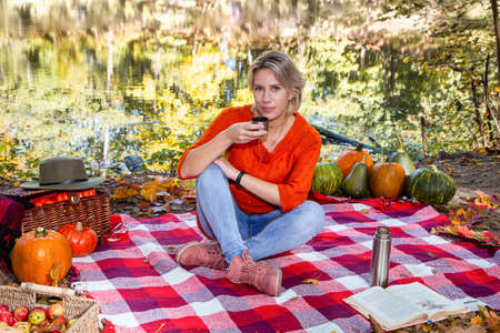 Young woman drinking hot tea from thermos in beautiful autumn forestの写真素材