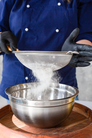 Woman sifting flour through old sieve on kitchen board