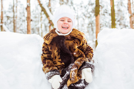 Winter portrait of cute smiling child girl on the walk in sunny snowy forest