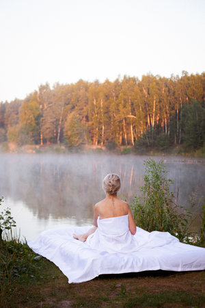 woman sleeping on a mattress with white sheets against the water of the lakeの写真素材