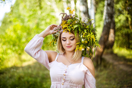 girl in a beautiful wreath walks through the summer meadowの写真素材