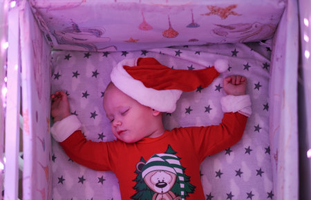 Toned photo of newborn baby dressed in Santa costume lying with Christmas gifts