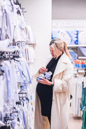 Young pregnant woman choosing newborn clothes at baby shop store. High quality photoの写真素材