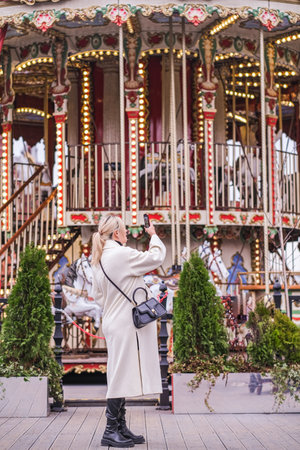 Stylish pregnant woman in a trendy white dress posing outdoors on the background of carousels. . High quality photoの写真素材