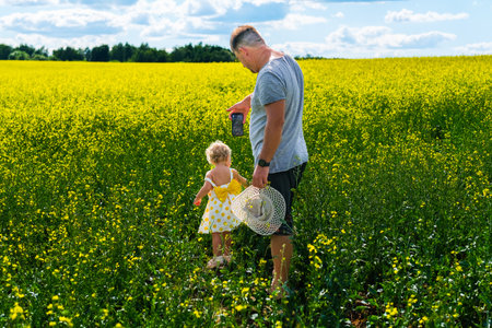 Dad filming his daughter on his phone in a field on a bright summer day. High quality photoの写真素材