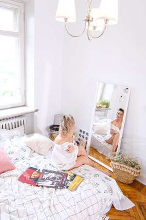 a beautiful blonde in a white shirt looks at her reflection in a mirror. High quality photoの写真素材