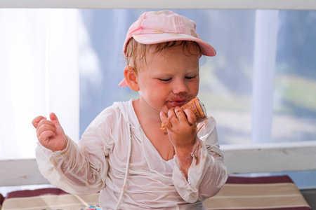 A young child is eating an ice cream cone while wearing a white shirt. The child is smiling and he is enjoying the treatの写真素材