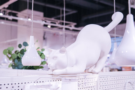 A white cat statue is on display in a store. The cat is looking down and he is in a playful mood. The store is decorated with white and green items, giving it a clean and fresh lookの写真素材