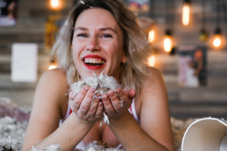 A woman is holding a pile of feathers and smiling. Scene is lighthearted and playfulの写真素材