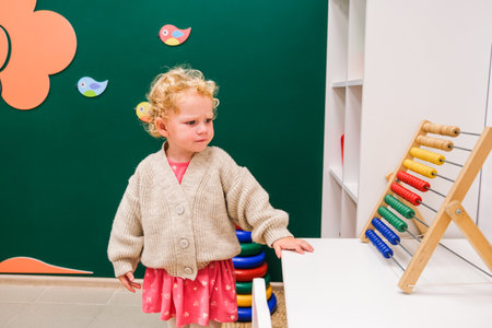 A young girl is standing in front of a wooden counting game. She is wearing a pink dress and a white sweaterの写真素材