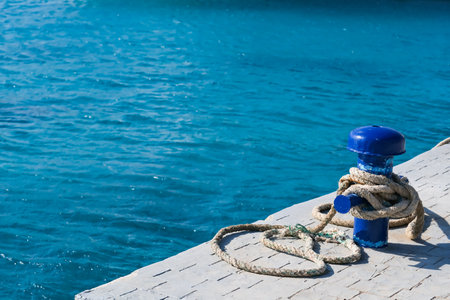A blue buoy sits on a dock in the ocean. The water is calm and blue. The buoy is tied to a rope,...