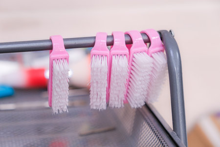 A row of five pink and white brushes are hanging on a metal rod. The brushes are all the same size and color, and they are arranged in a neat row. Concept of organization and cleanlinessの写真素材