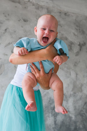 A woman is holding a baby in her arms. The baby is crying and the woman is trying to comfort him