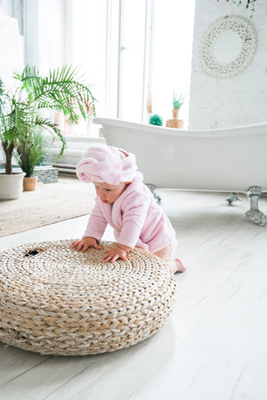 A baby in a pink robe is playing on a round rug. The baby is wearing a towel and he is enjoying the activityの写真素材
