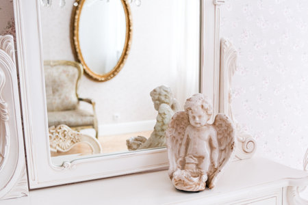 A white dresser with a mirror and a statue of an angel on top. The room is decorated in a classic style with a lot of white and gold accentsの写真素材