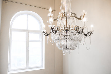 A chandelier hangs above a window, casting a warm glow on the room. The chandelier is made of...