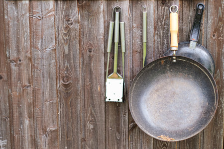 A wooden fence with a pan and spatula hanging on it. The pan is old and the spatula is greenの写真素材