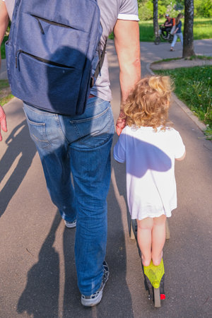 moscow, russia, 05/24/2025 A man and a child are walking down a path with a backpack on the man's back. The child is riding a scooterの写真素材