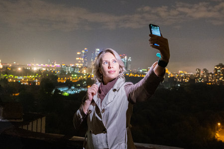 woman makes selfie on her smart phone on night city background