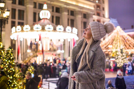 moscow, russia, 01/12/2020 Caucasian woman enjoying Christmas market outdoor during holiday season. Winter festival scene with carousel and blur lights. Merry Christmas concept.の写真素材