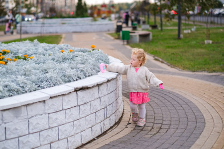 moscow, russia, 09.28.2024 Little girl with curly hair walking near a flower bed in a park. Learning to walk concept. Toddler exploring outdoors.の写真素材