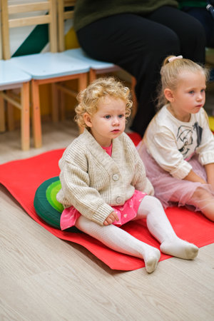 moscow, russia, 09.28.2024 A little, blonde, caucasian girl is sitting on a red mat in a room. Child development and early learning concept for kindergarten and preschool education.の写真素材