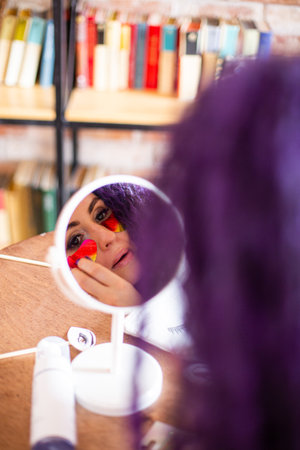 Woman with colorful face paint looking in mirror. Creative makeup application for festive occasions....