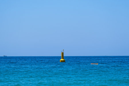 Yellow buoy floating on blue sparkling sea water under clear sky with ship in distance. Summer...