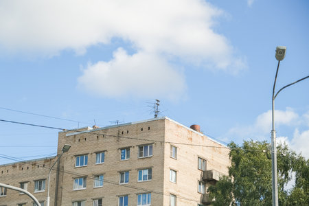 Russia, Saint Petersburg, 08/23/2025 Residential building with brick facade and antenna on roof under blue sky, electricity lines, light pole, tree, daytime scene representing city life and architecture.の写真素材