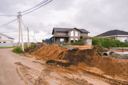 Russia, Saint Petersburg, 08.23.2025 Private house construction in suburban area for family resident. New modern home facade surrounded by building materials and dirt piles.の写真素材