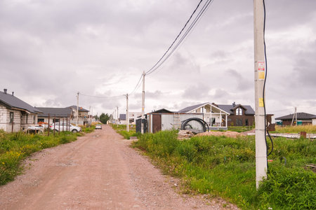 Russia, Saint Petersburg, 08.23.2025 Unfinished suburban country road with new private houses under construction on cloudy day, showing the development process.の写真素材