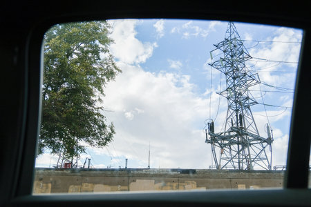 Russia, Saint Petersburg, 08/23/2025 View from car window of a power line tower and tree against a...