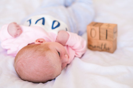 Newborn caucasian baby lying on white blanket with one month wooden photo prop. Infant age milestone concept. Childhood development.の写真素材