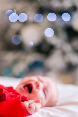Cute newborn baby girl in red sleeps on bed. Adorable infant child resting at home. New life, family love concept.の写真素材
