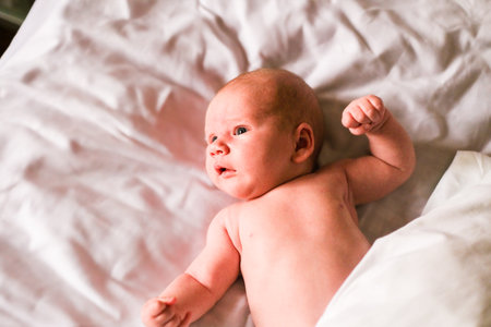 Adorable newborn baby boy lying on bed in neutral colored sheets. Child relaxing on soft bedding....