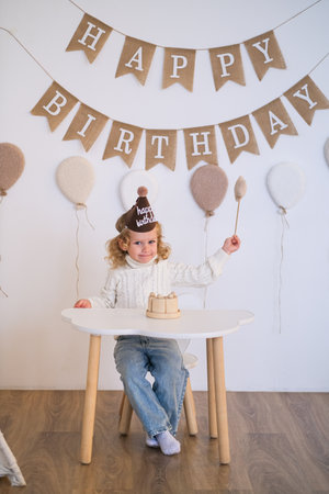 A cute caucasian child wearing a party hat sits at a small table with a mini cake for a first birthday celebration portrait.の写真素材