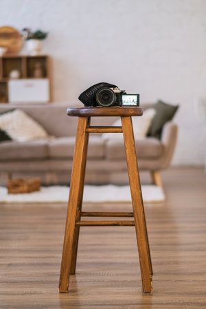 Digital camera sitting on wood stool. Photography equipment in studio setting. Creative craft and hobby. Technology in home environment.の写真素材