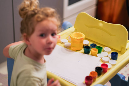 Young girl looking at camera with stack of blank paper and paint set. Creative art hobby for kid at home.の写真素材