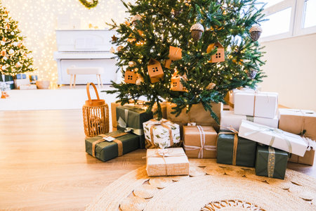 Christmas tree decorated with lights and house ornaments, surrounded by presents wrapped in craft paper and white boxes. Holiday celebration concept.の写真素材