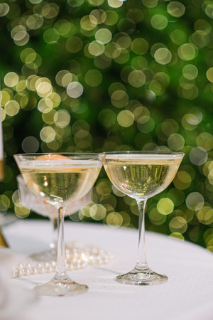 Two champagne glasses with sparkling wine on a white table with blurred green bokeh lights in the background for celebration of Christmas or New Year.の写真素材