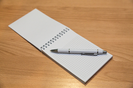A notebook and ballpoint pen lying on a wooden table.の写真素材