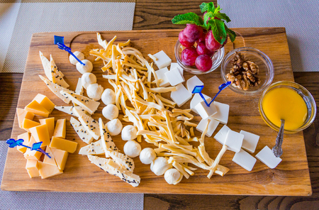 Cheese plate in the restaurant. Different varieties of cheese on a wooden tray. Honey, grapes and walnutsの写真素材
